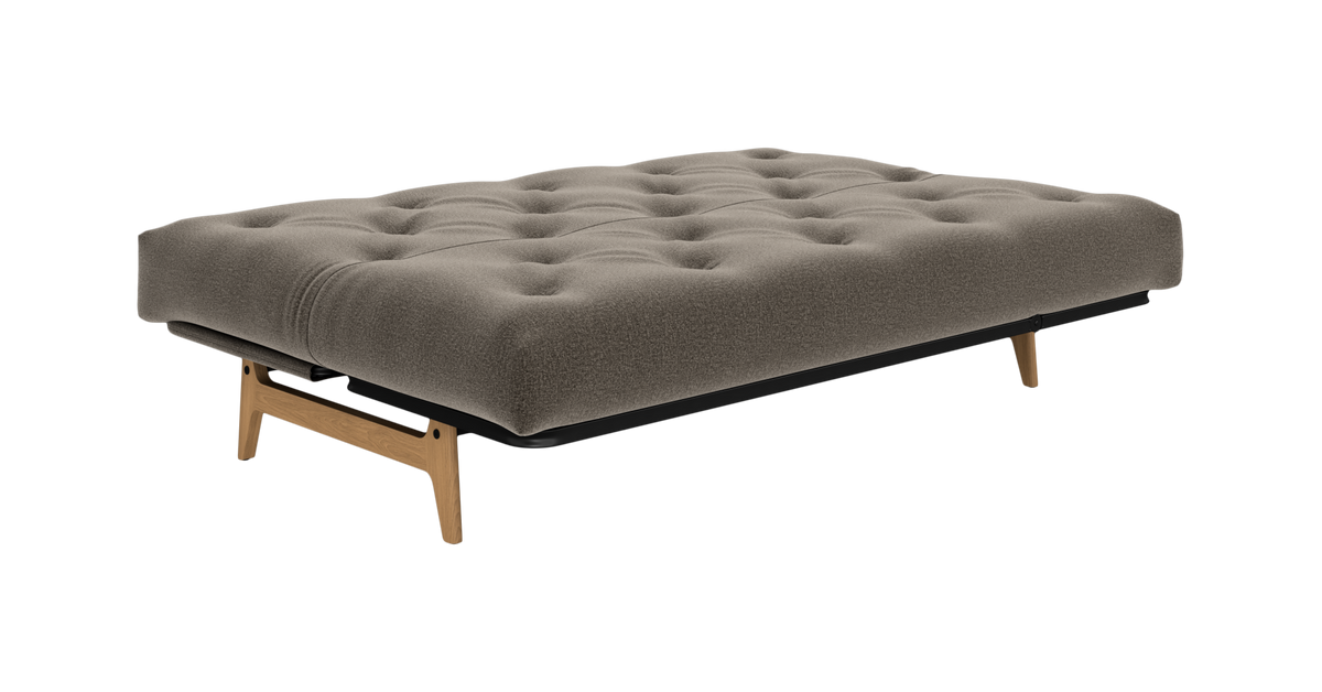 Beige, tuftet futon/udslået sovesofa med sort ram og træben, frilagt på hvid baggrund.