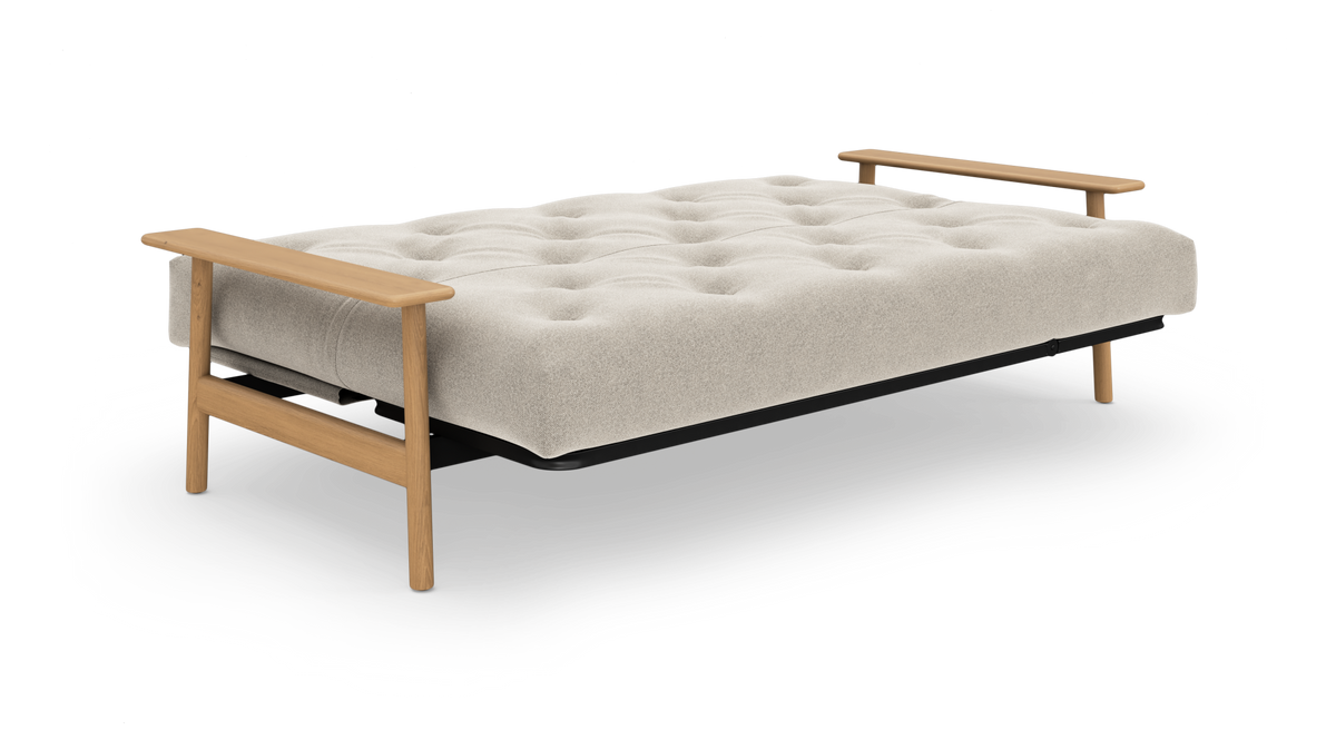 Beige sovesofa i udslået position med tuftet madras, sorte kanter og lyse træarmlæn og ben.