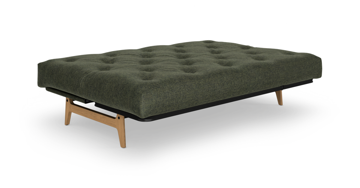 Grøn sovesofa/futon med tuftet madras og træben, frilagt på hvid baggrund.