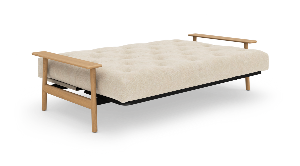 Beige sovesofa med tuftet madras og lyse træarmlæn, frilagt på hvid baggrund.