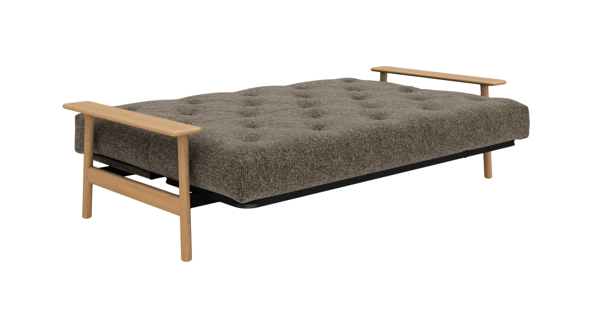 Brungrå sovesofa i udslået position med knapquiltet madras og lyse træarmlæn, frilagt på hvid baggrund.