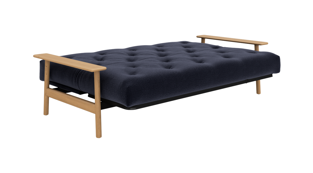 Mørkeblå sovesofa med knapstukket madras og lyse træarmlæn, fritlagt produktbillede.
