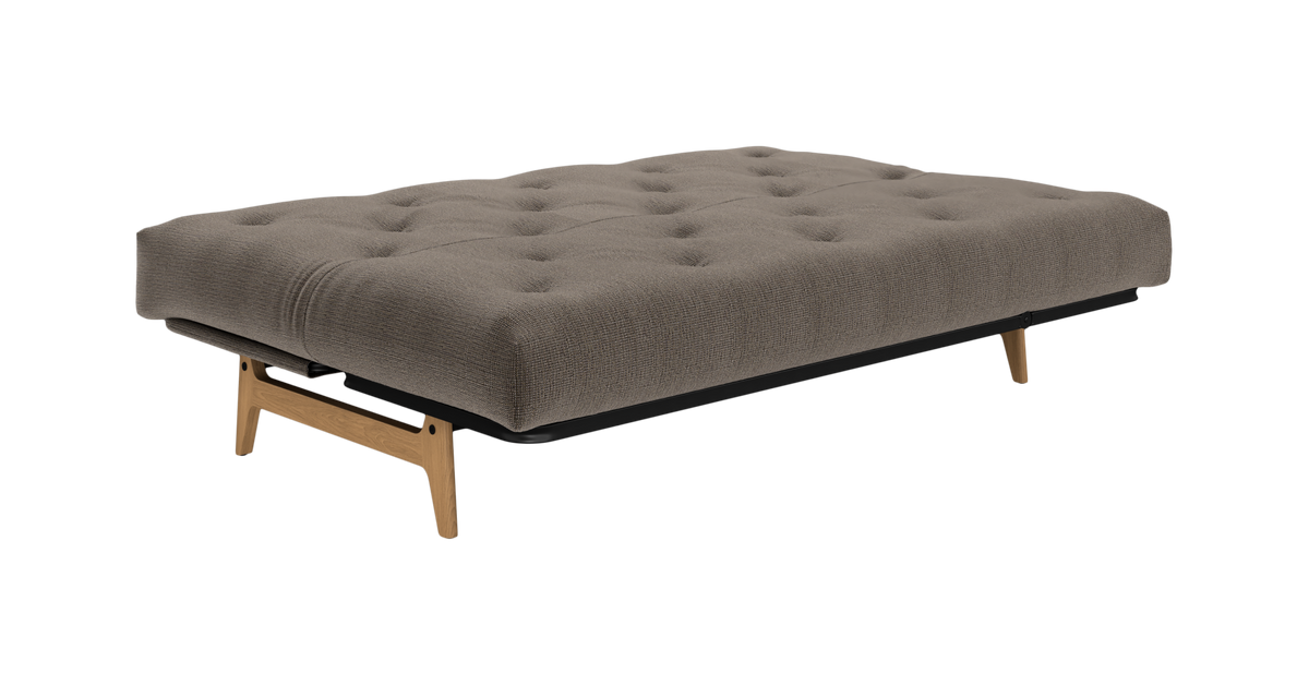 Lav futon/sovesofa-modul med knapstukket taupegrå madras og træben, frilagt på hvid baggrund.