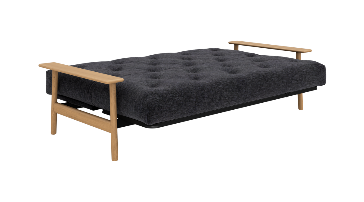 Mørkegrå sovesofa/futon med tuftet madras og lyse træarmlæn, frilagt på hvid baggrund.