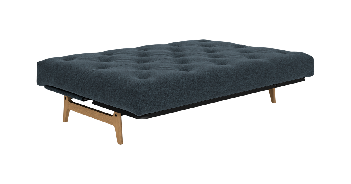 Mørkeblå udslået sovesofa/futon med tuftet madras og træben, set skråt forfra på hvid baggrund.