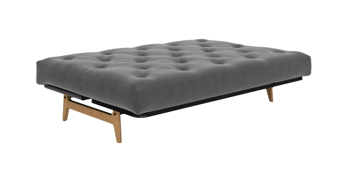 Grå, tuftet sovesofa/daybed med træben, fritlagt på hvid baggrund set skråt forfra.