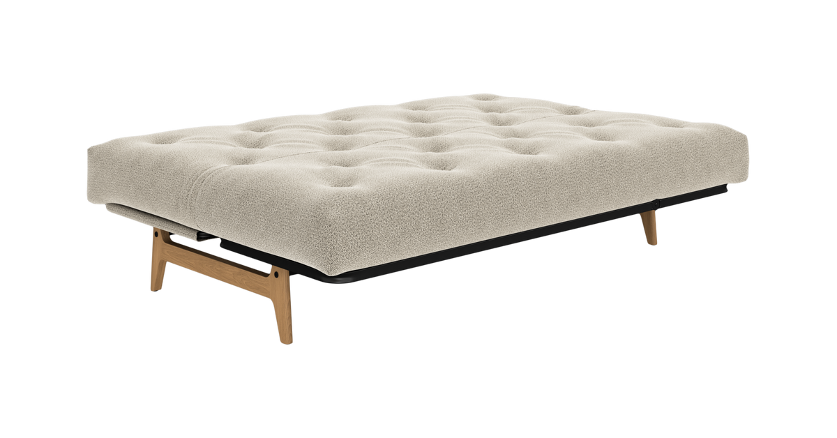 Beigefarvet sovesofa/futon med tuftet madras og træben, fritlagt på hvid baggrund.