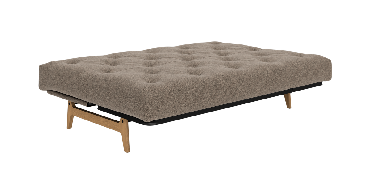 Beige sovesofa i udslået position med tuftet madras og træben, frilagt på hvid baggrund.