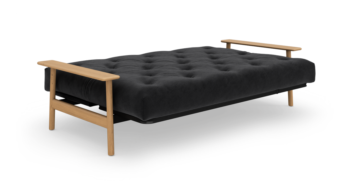 Sort sovesofa i udslået position med tuftet madras og lyse træarmlæn og ben.