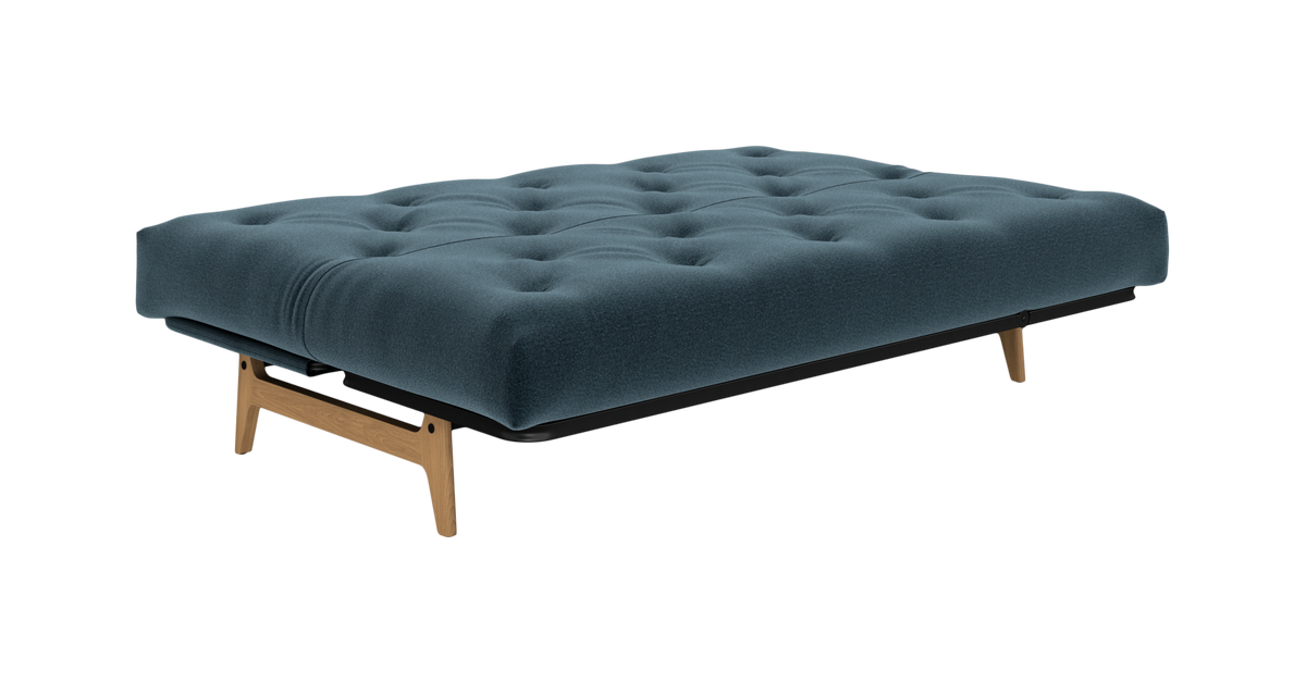 Blå knappet sovesofa/futon med træben, frilagt produktfoto i vinkel.