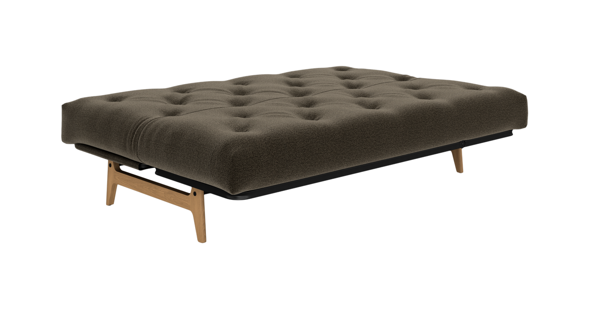 Olivengrøn knapquiltet futon/dagbed med træben, frilagt på hvid baggrund i skrå vinkel.
