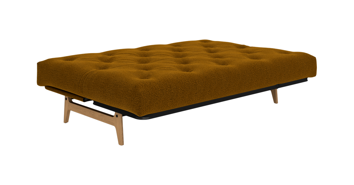 Lav sovesofa/daybed i sennepsgul bouclé med tuftet sæde og træben, fritlagt på hvid baggrund.