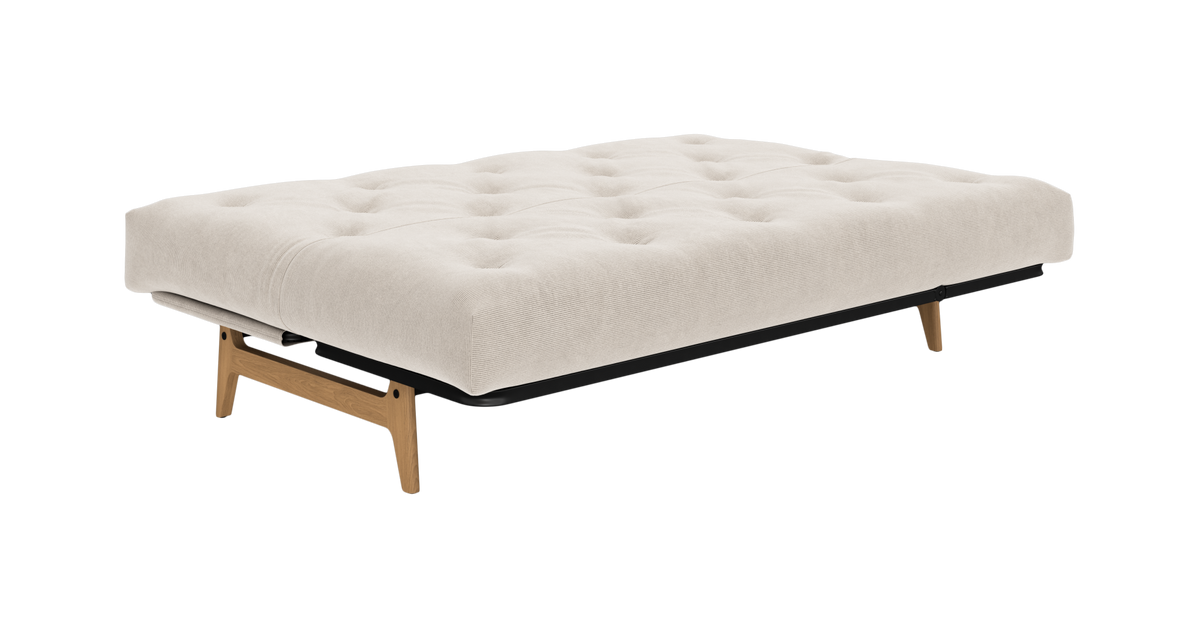 Beige, tuftet sovesofa/futon med træben, fritlagt på hvid baggrund.