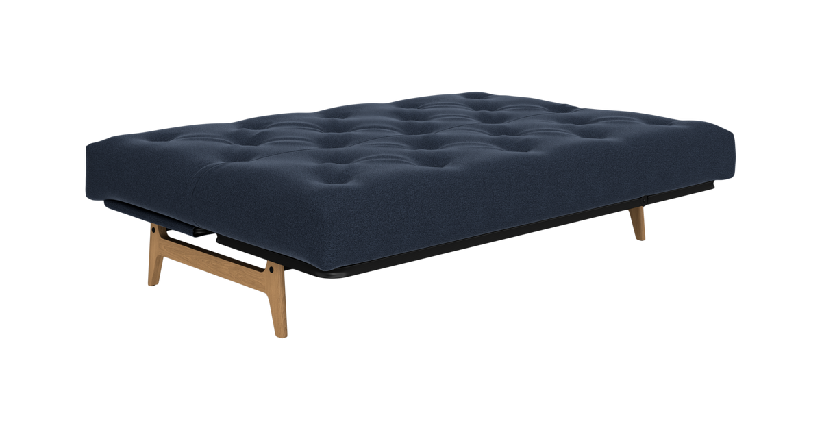 Mørkeblå sovesofa/futon med knapstoppet madras og træben, frilagt på hvid baggrund.