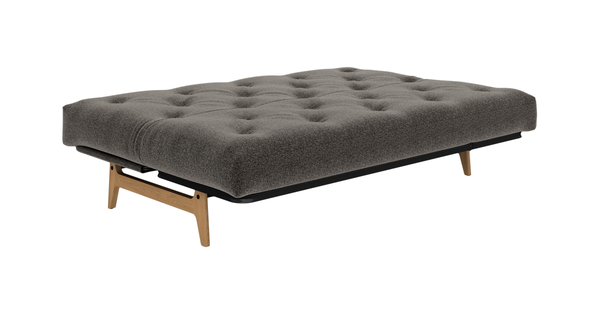 Grå tuftet futon/dagbed med træben, frilagt på hvid baggrund.
