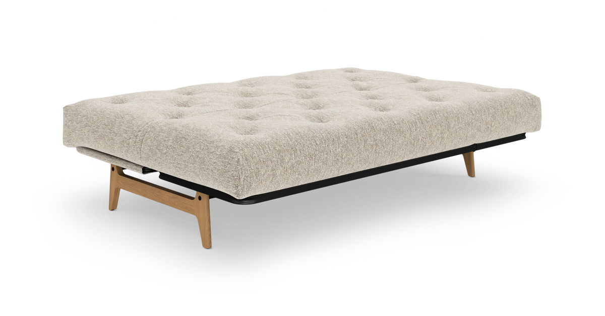 Beige sovesofa med tuftet madras, træben og sort ramme på hvid baggrund.