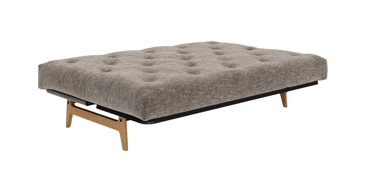 Grå tuftet sovesofa/futon med træben på hvid baggrund.