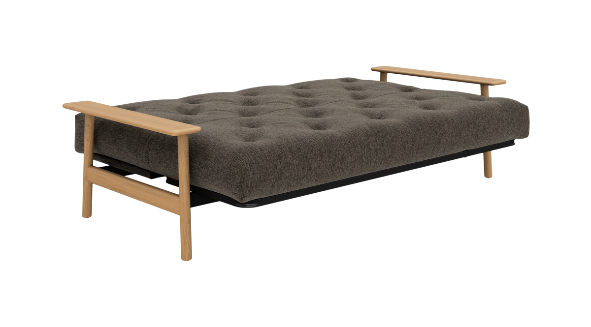 Grå polstret sovesofa/daybed med knapstikning og lyse træarmlæn, frilagt på hvid baggrund.