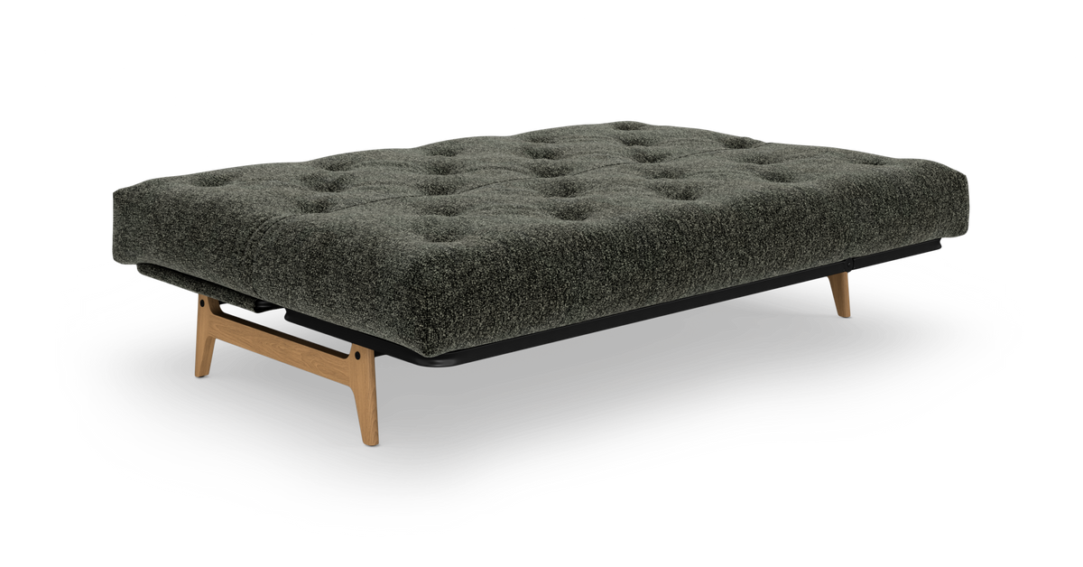 Mørkegrøn tuftet sovesofa/futon med træben, frilagt på hvid baggrund.