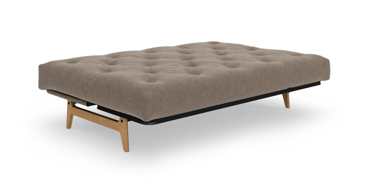 Beige sovesofa/daybed med tuftet madras, træben og sort ramme, frilagt på hvid baggrund, set skråt forfra.