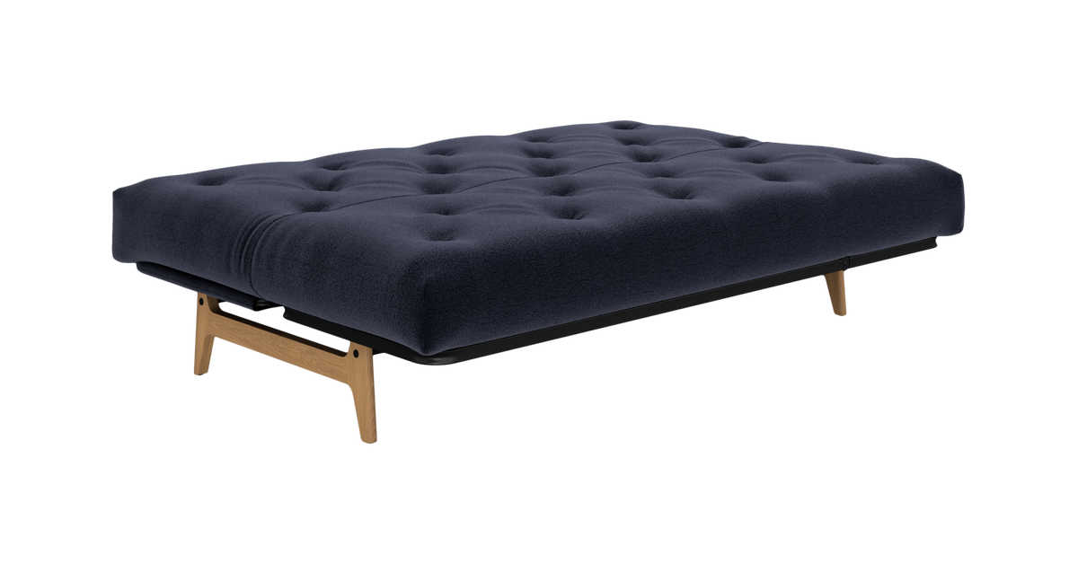 Mørkeblå tuftet sovesofa i udslået sengeleje med træben, frilagt produktfoto.