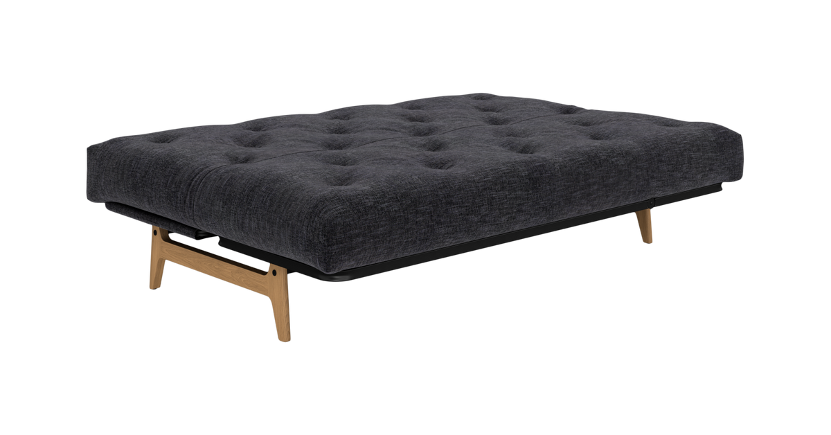 Mørkegrå, knapquiltet sovesofa med træben, fritlagt på hvid baggrund.