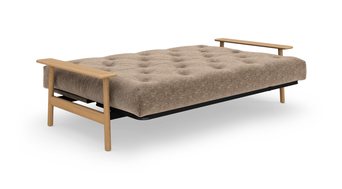 Beige sovesofa med knapquiltet madras og lyse træarmlæn.