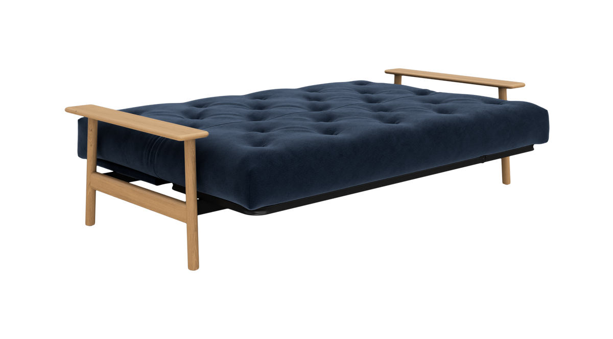 Mørkeblå, tuftet sovesofa med træarmlæn og -ben, frilagt på hvid baggrund.