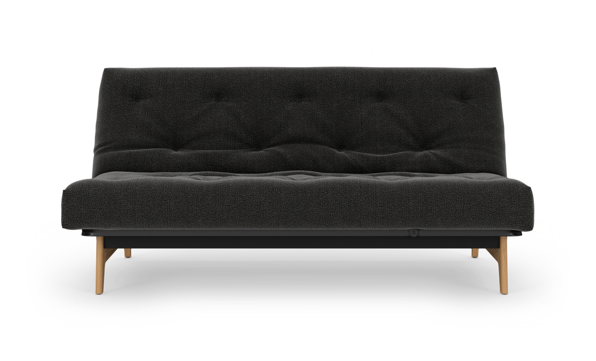Mørkegrå sovesofa med tuftet polstring og træben, fritlagt forfra.