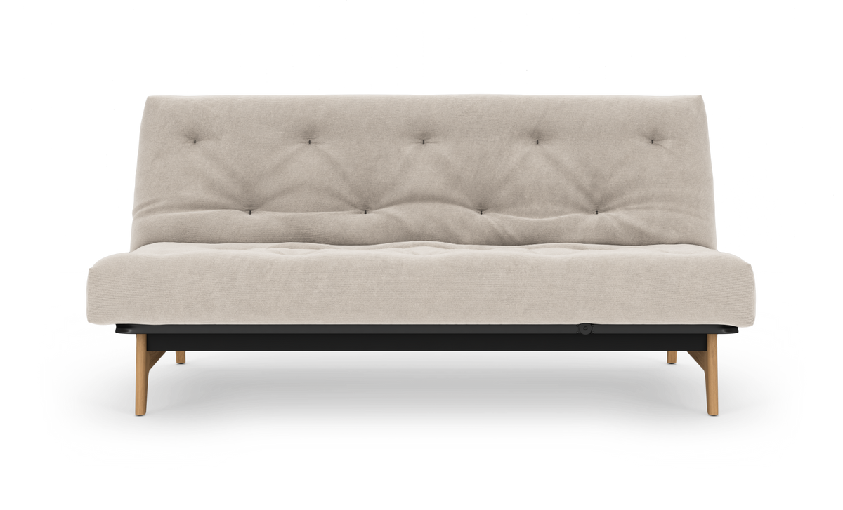Beige sovesofa med tuftet ryglæn, træben og sort base, frilagt på hvid baggrund.