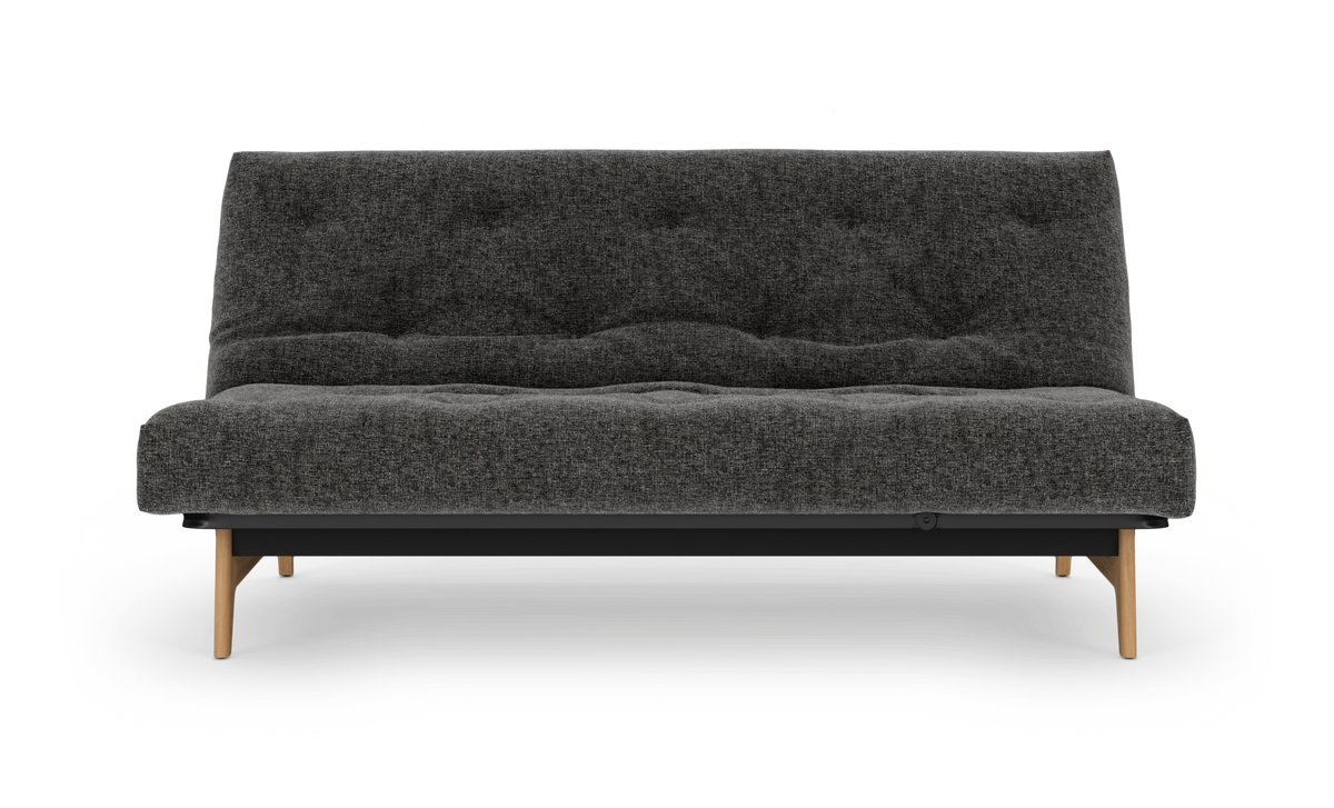Mørkegrå stofsofa med knapper og træben set forfra på hvid studiobaggrund.