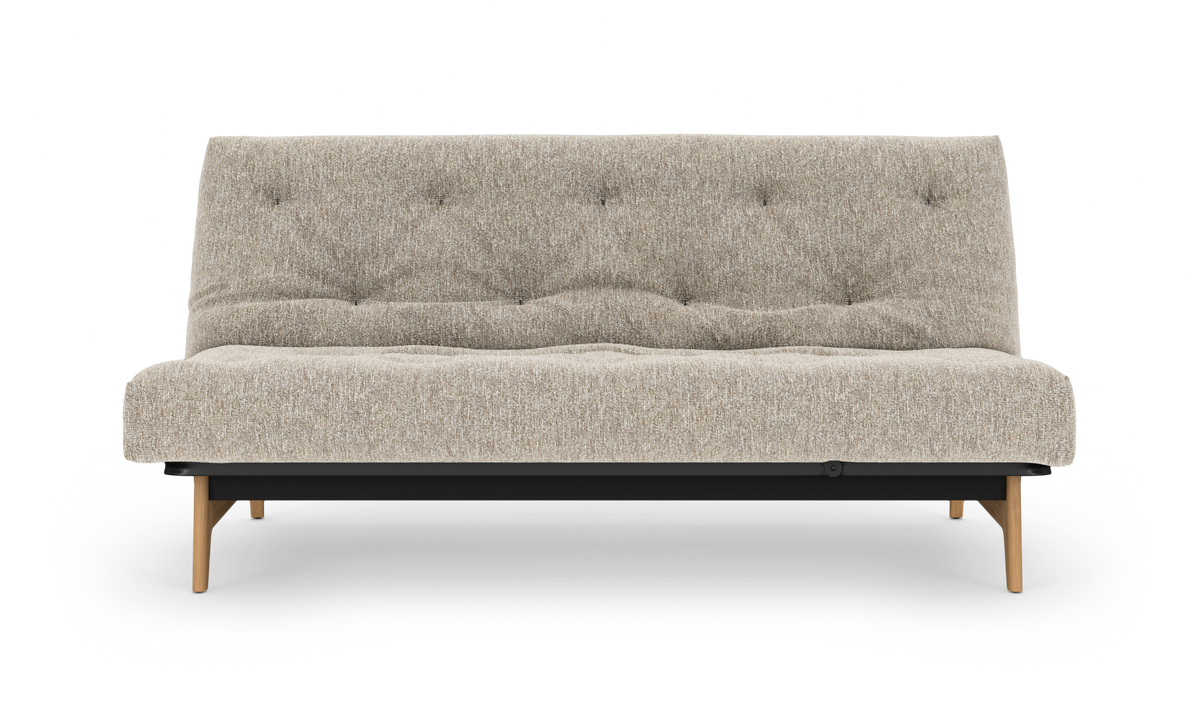 Beige sovesofa med tuftet polstring, træben og sort base, fotograferet forfra på hvid baggrund.