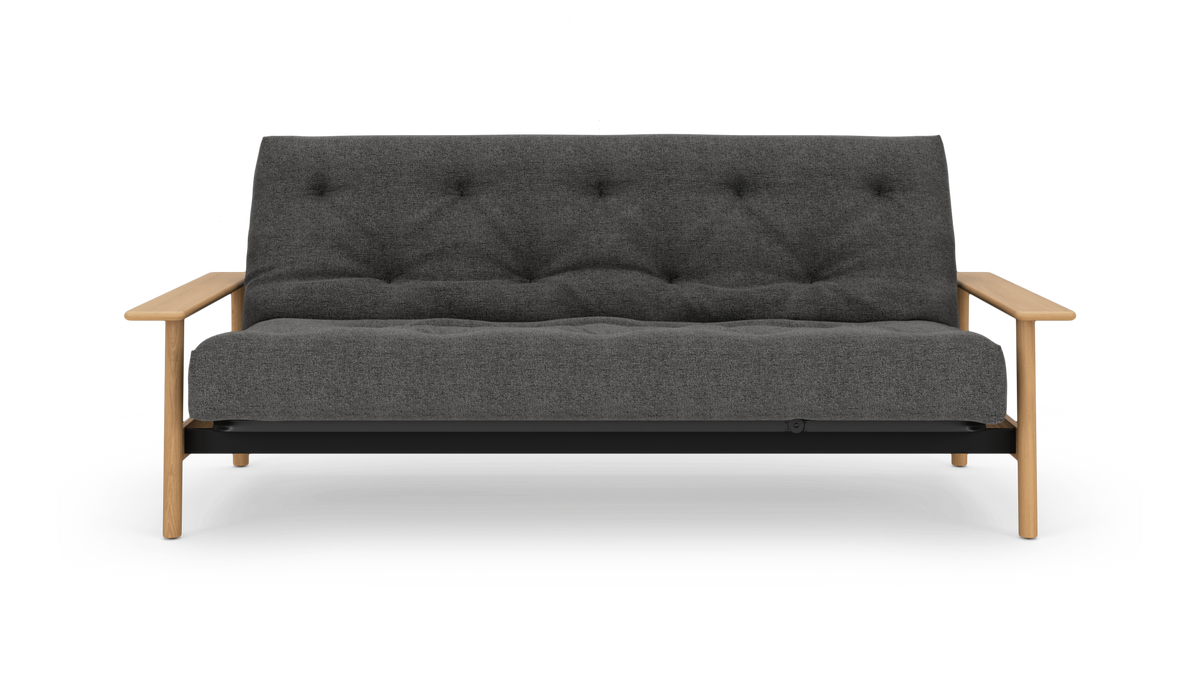Mørkegrå, vatteret sofa med lyse træarmlæn og ben, set lige forfra på hvid baggrund.