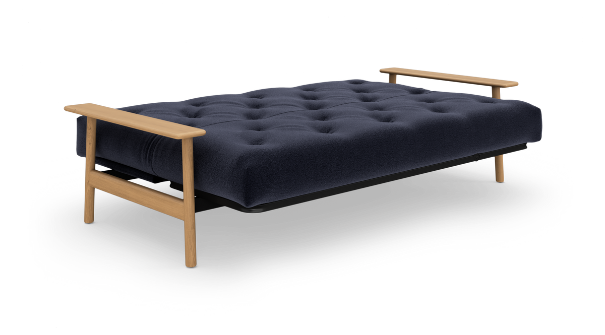 Mørkeblå, tuftet sovesofa med træarmlæn og ben, fritlagt på hvid baggrund.