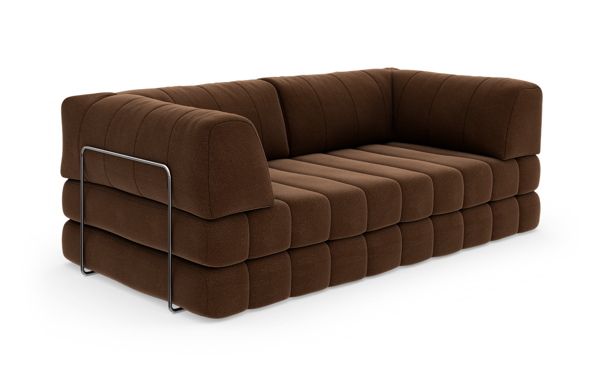Brun, blød modulsofa med brede, kviltede hynder og en slank metalbøjle som detalje på siden, fritlagt på hvid baggrund.