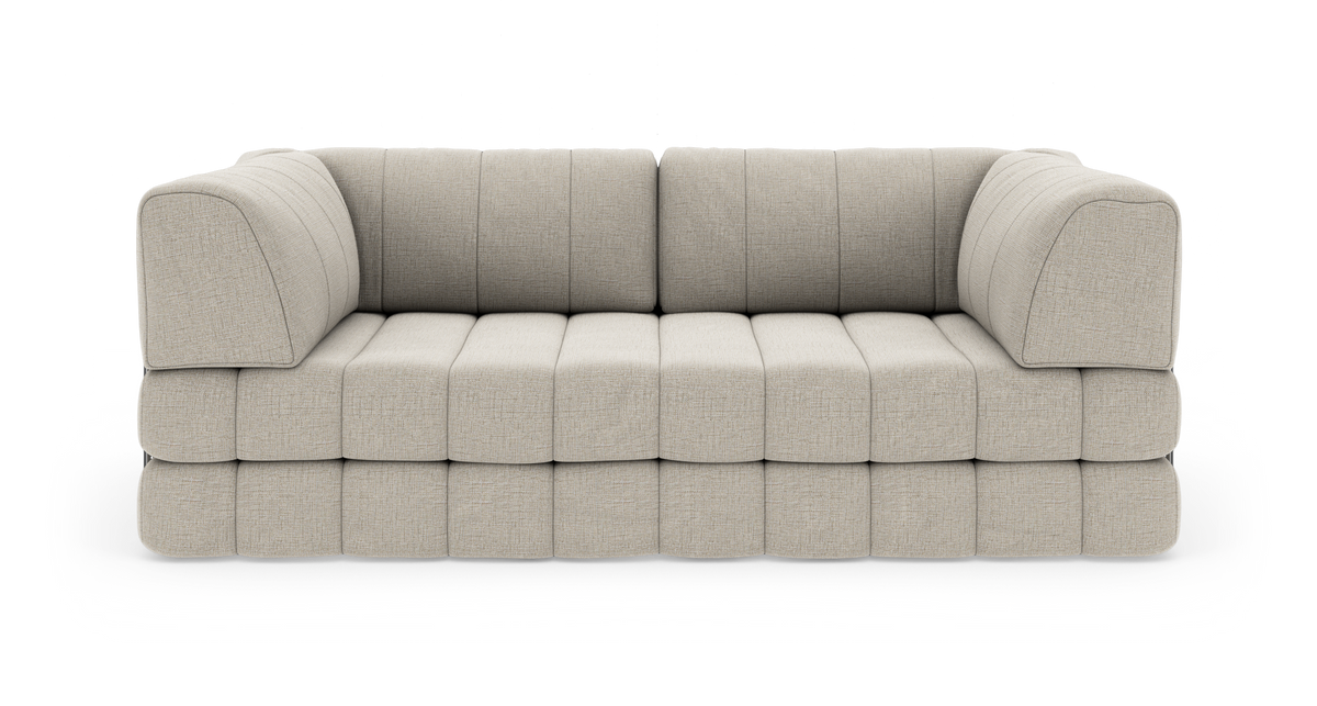 Beige modulsofa i stof med bløde kanter og quiltet sæde, fotograferet lige forfra mod hvid baggrund.