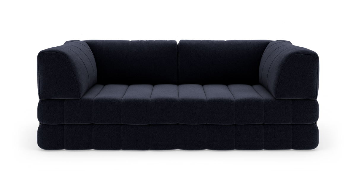 Mørkeblå, lav modulær 3-personers sofa med afrundede armlæn og dybe kanal-/blokopdelte sædehynder, frilagt på hvid studiebaggrund, frontvisning.