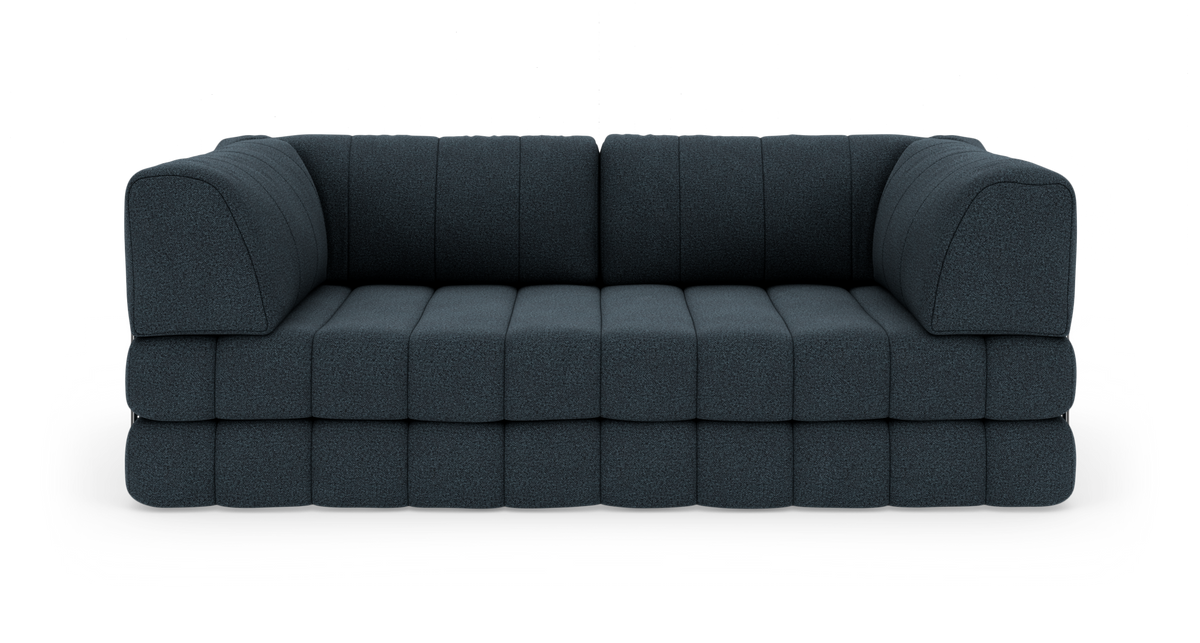 Modulsofa i mørkeblåt stof med lave, brede sædehynder, fotograferet lige forfra på hvid studiebaggrund.