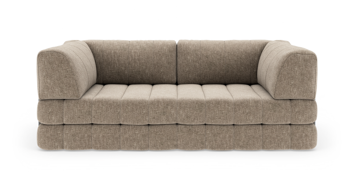 Beige modulsofa i stof med bløde, afrundede armlæn og quiltet sæde, vist forfra i studiopsætning.