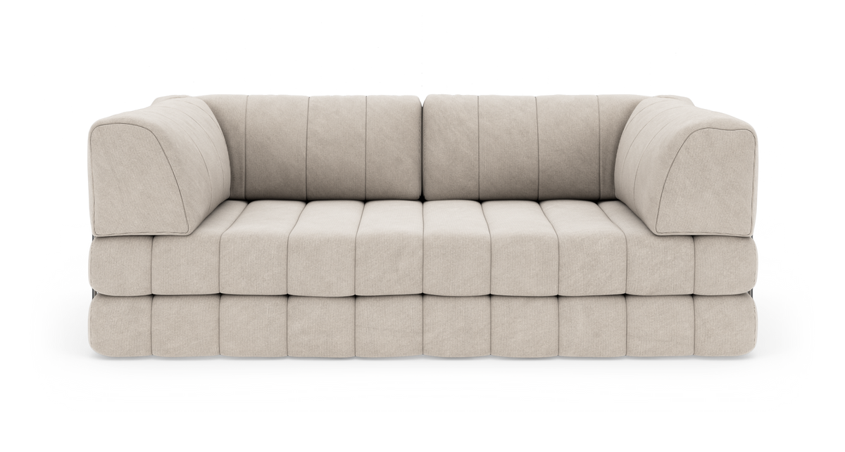 Beige modulsofa med kraftigt polstrede blokpuder og afrundede hjørner, frilagt på hvid baggrund.