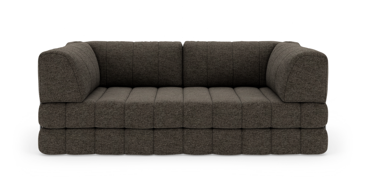 Modulsofa i mørkegrå/brun tekstil med dybe sæder og afrundede armlæn, set lige for i studiemiljø.