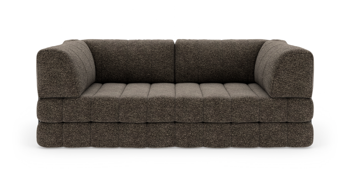 Brungrå stofsofa med brede, quiltede sædehynder og afrundede armlæn, fritlagt på hvid baggrund.