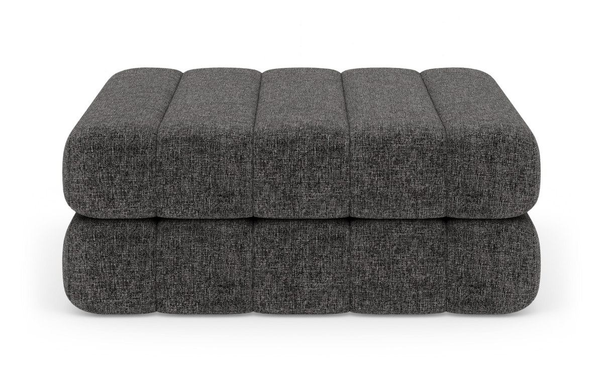 Mørkegrå, stofbeklædt modulær puff/ottoman set forfra i studiemiljø.