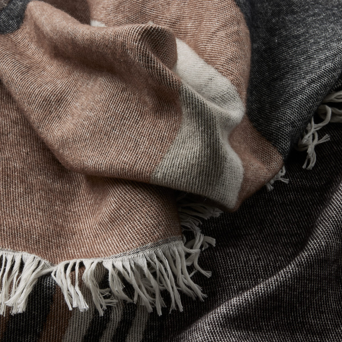 Nærbillede af et blødt plaid med frynser i beige, grå og creme.