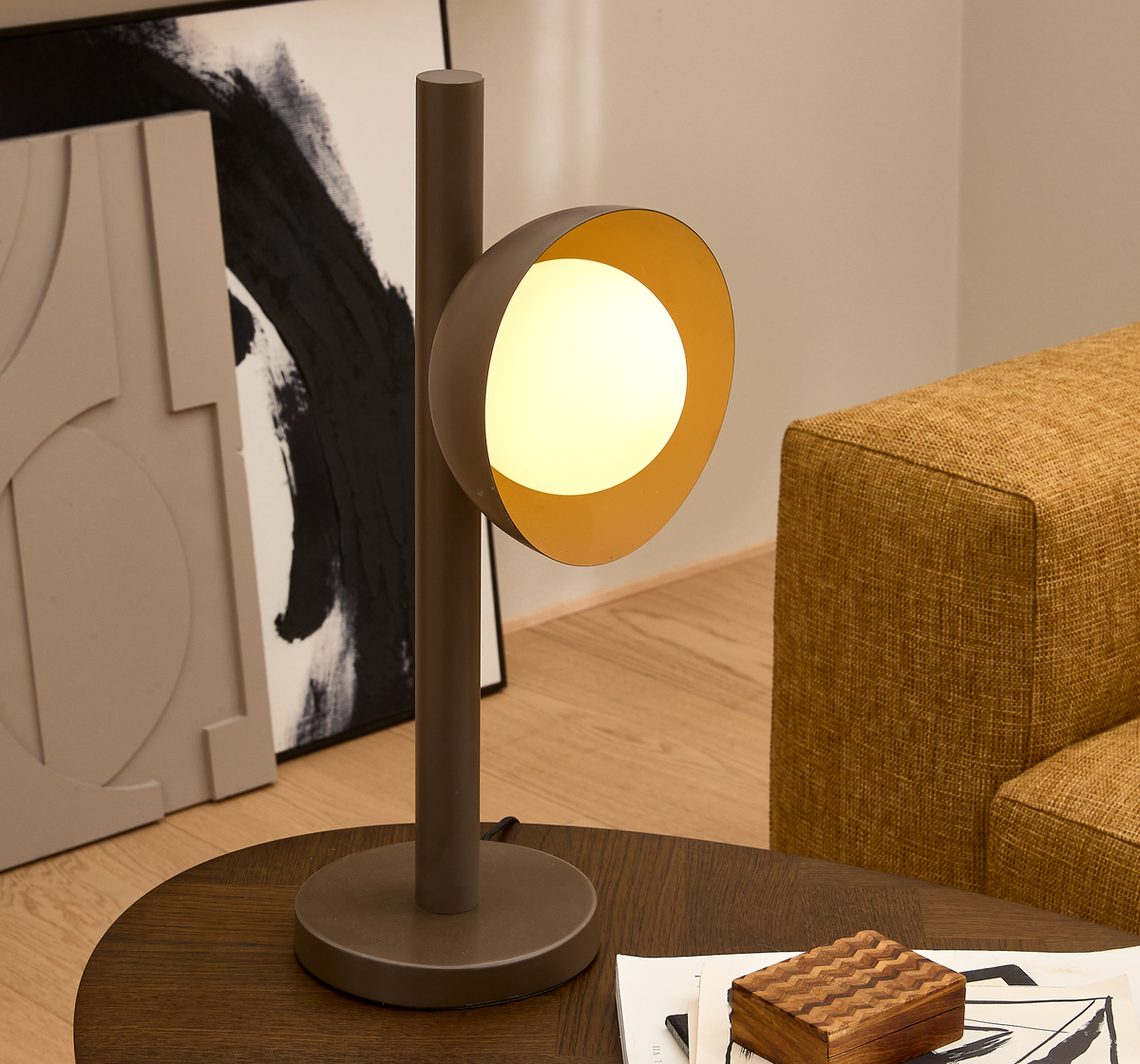 Moderne bordlampe med varm glød på et mørkt træ-sofabord i en stue, med abstrakt kunst i baggrunden og sennepsgul sofa.