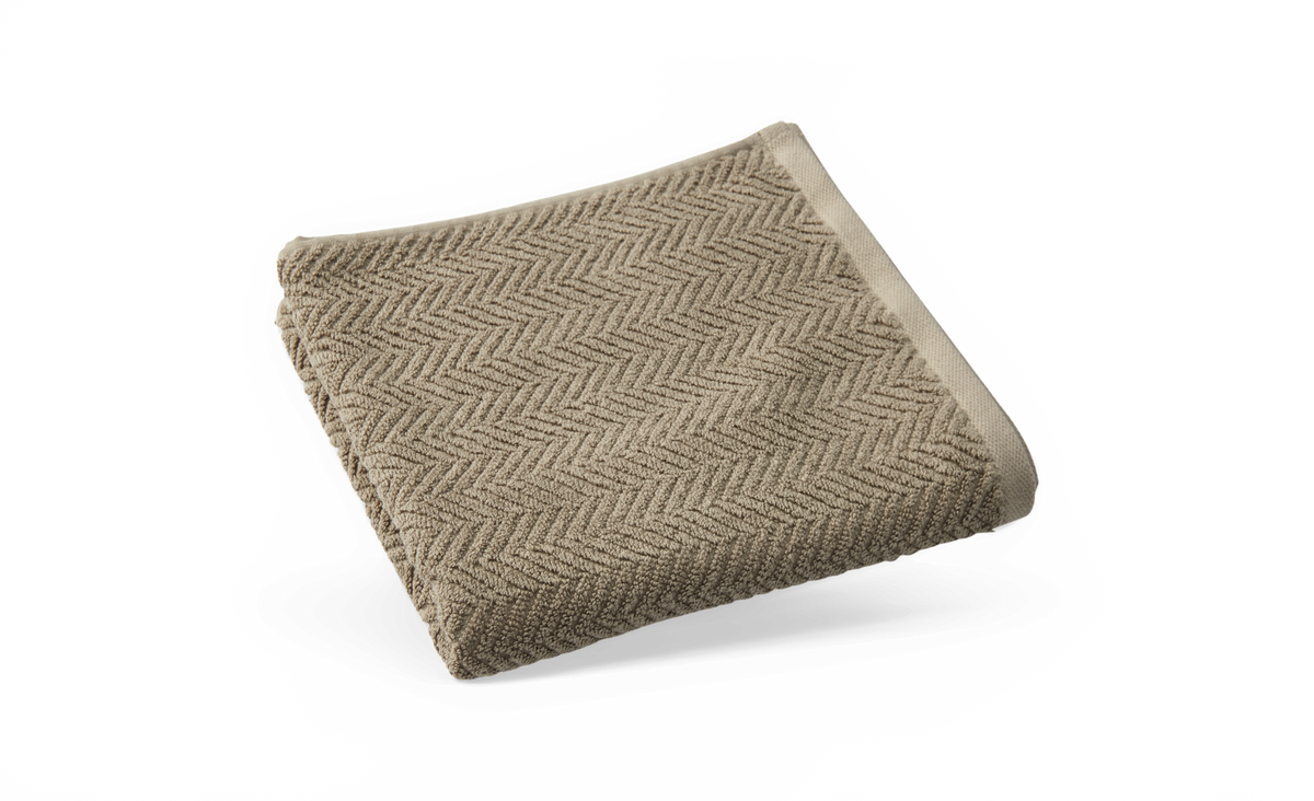 Sammenfoldet beige håndklæde med sildebenmønster på hvid baggrund.