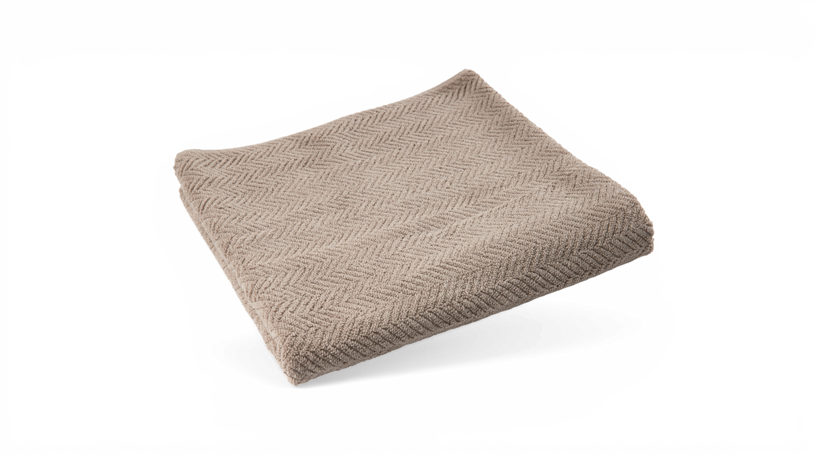 Beige håndklæde med sildebensmønster, foldet fladt på hvid baggrund.