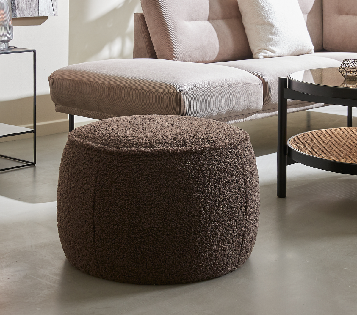 Brun rund bouclé‑puf foran en beige sofa og rundt sofabord i en lys stue.