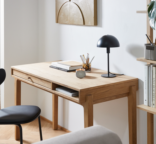 Minimalistisk hjemmekontoropstilling med egetræsskrivebord, sort bordlampe, stol og penneholder; bøger inklusiv The Kinfolk på hylden.