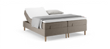 Justerbar dobbeltseng med hævet hovedende, beige polstret base, hvid topmadras samt gråt plaid og pude._ps